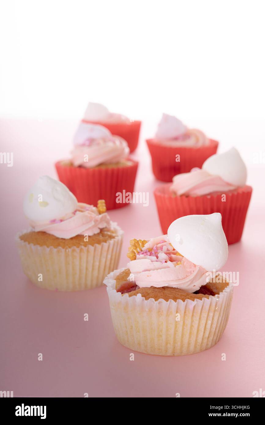 Sei cupcake alla vaniglia con glassa rosa, meringa bianca e pezzi di cono per waffle, disposti su una superficie rosa chiaro in due file ordinati. Foto Stock