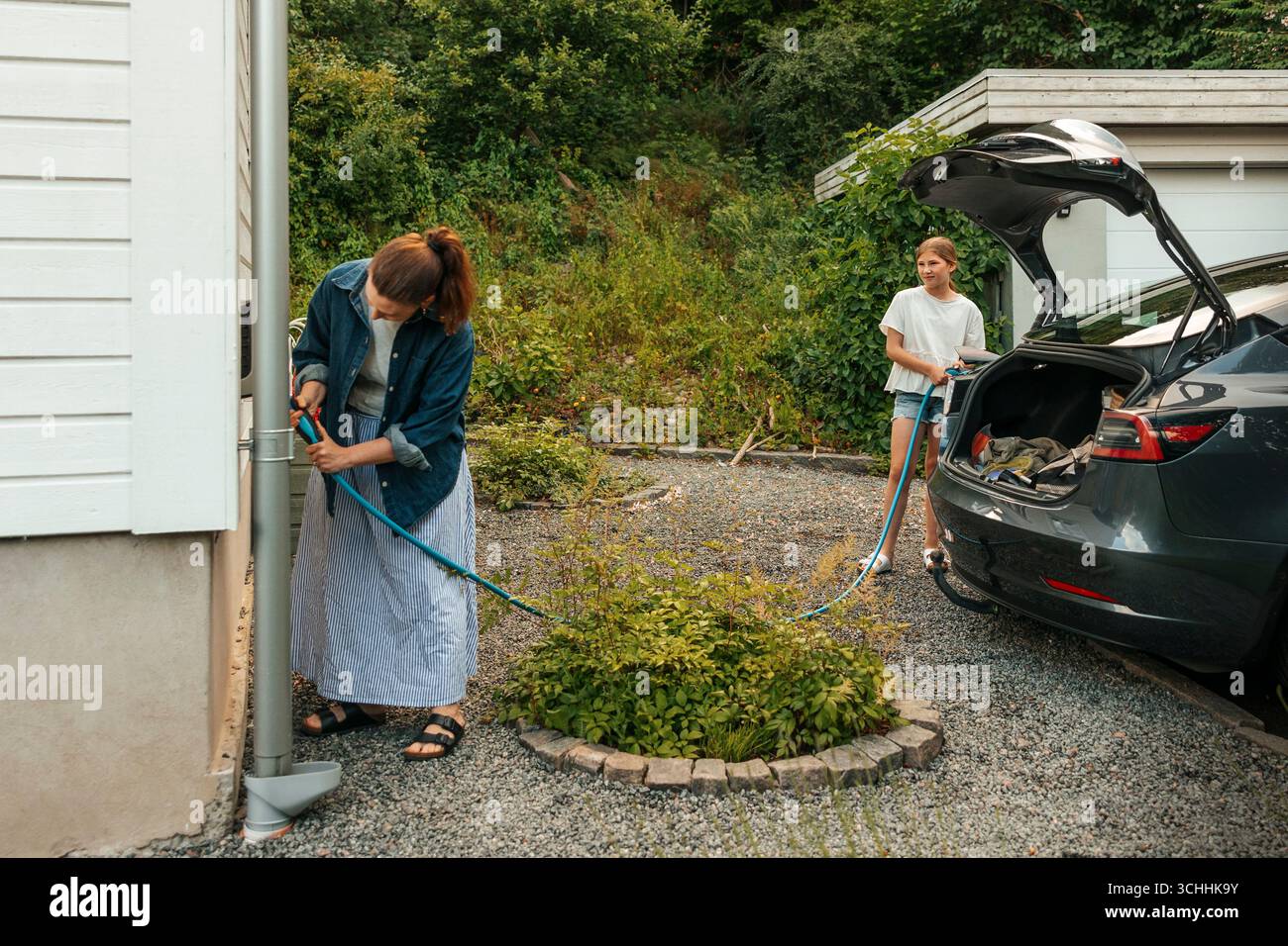 Madre e figlia caricano un'auto elettrica nel cortile posteriore Foto Stock