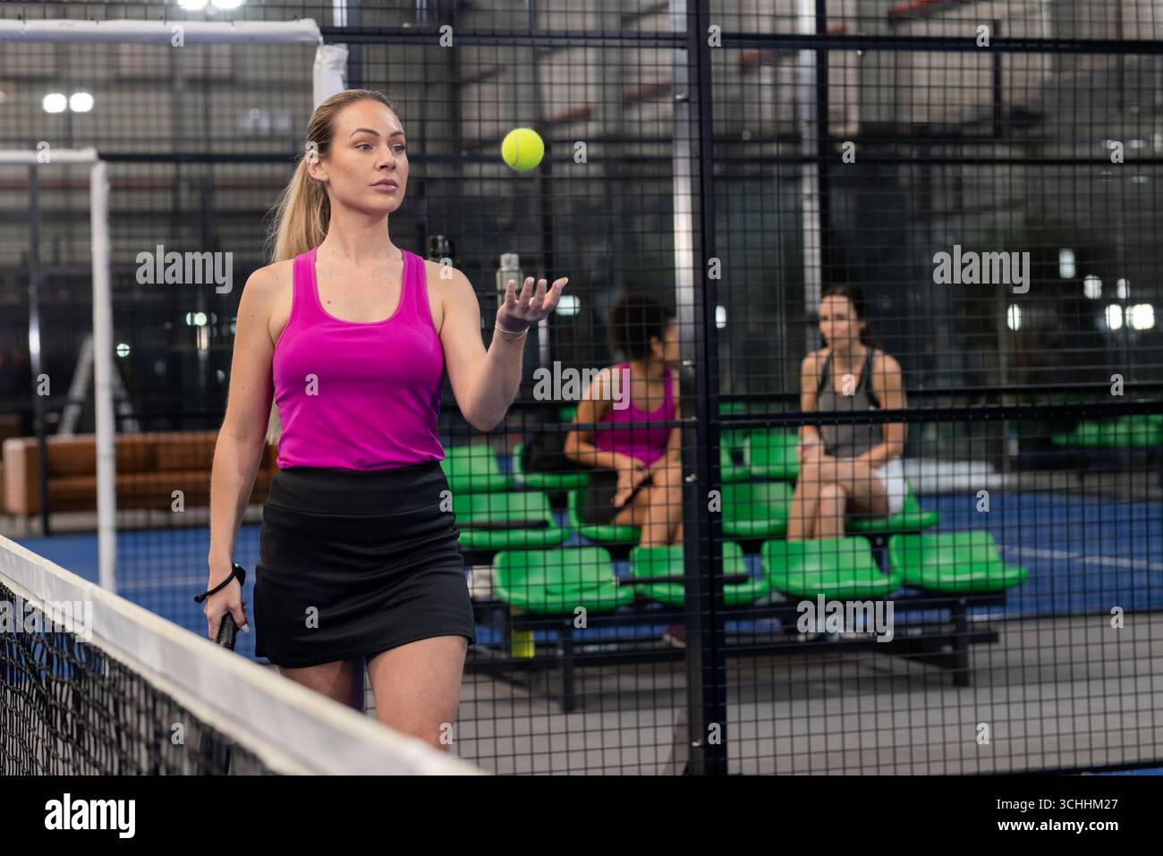 Diverse compagne di squadra che lanciano palla da tennis con una racchetta di padel accanto alla rete e alla rete Foto Stock