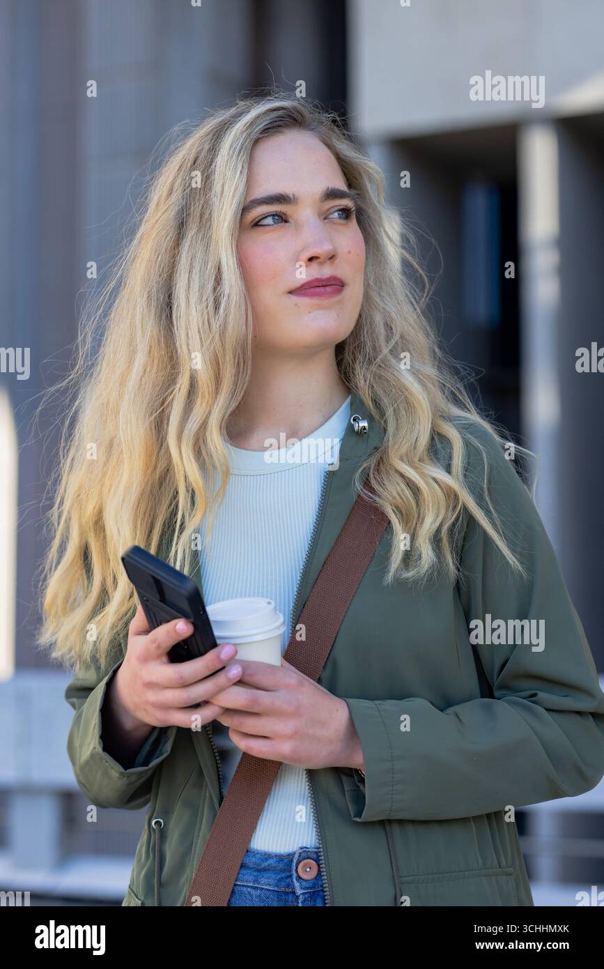 Donna all'esterno della piazza che indossa una tracolla con uno smartphone che guarda a destra Foto Stock