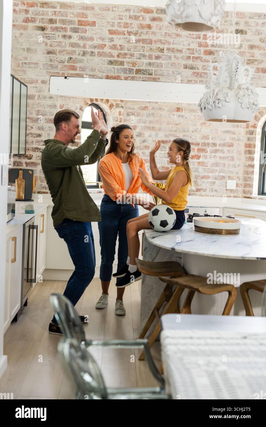 La famiglia festeggia in cucina, sorridendo e giocando a calcio sul bancone Foto Stock
