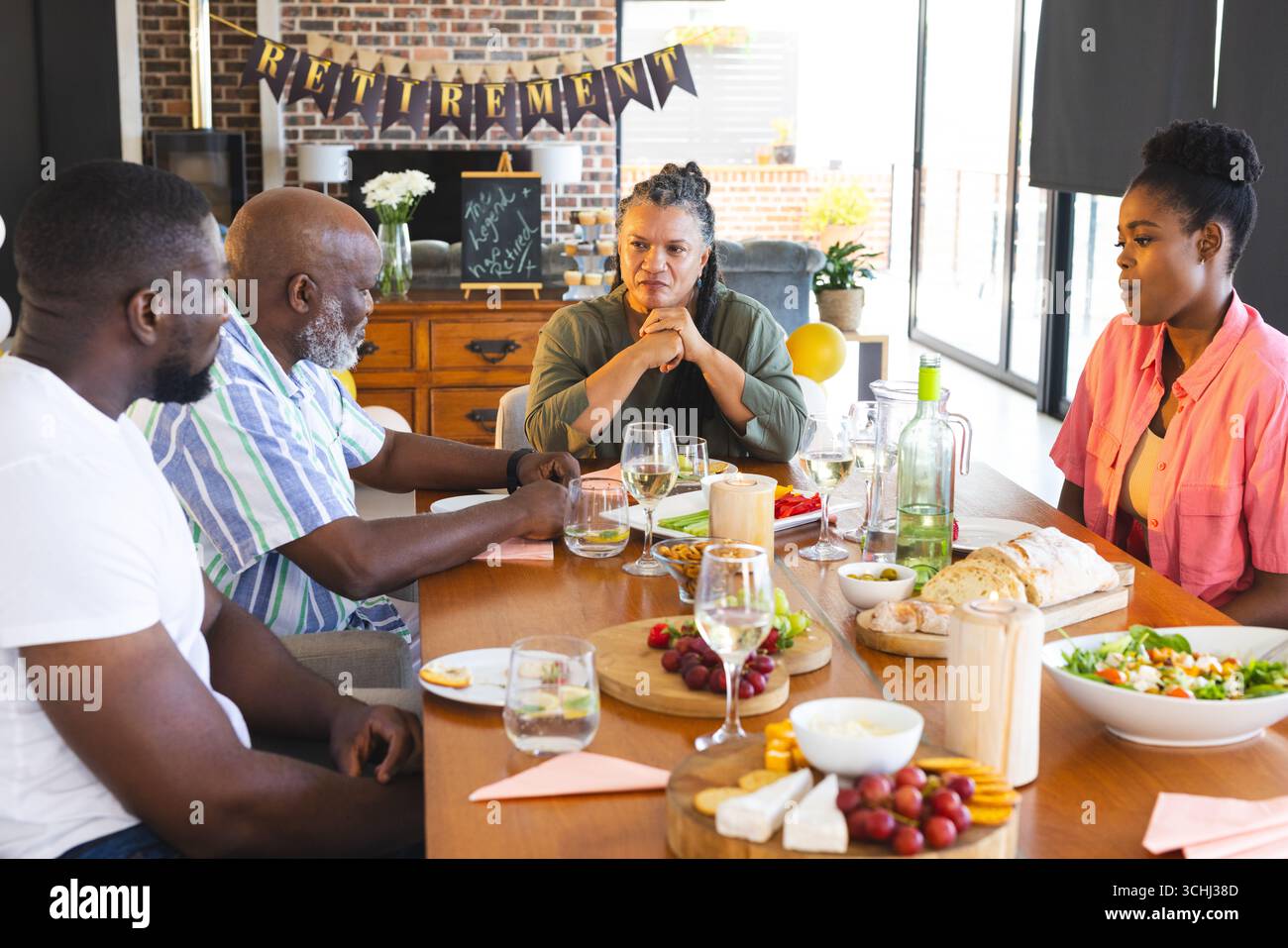 Famiglia che festeggia la pensione con cibo e bevande, condividendo storie a tavola Foto Stock