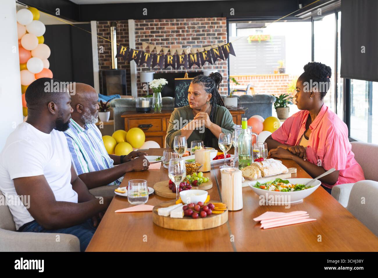 Famiglia che celebra la pensione con cibo e bevande, condividendo storie a casa Foto Stock