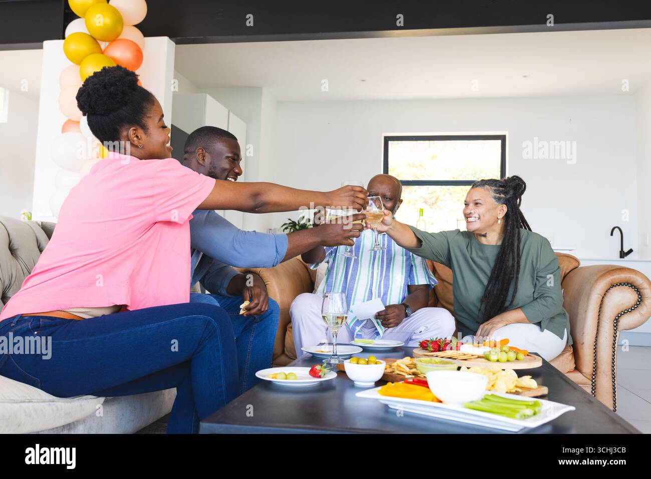 Gli amici brindano con bevande a casa, festeggiano con spuntini e risate Foto Stock