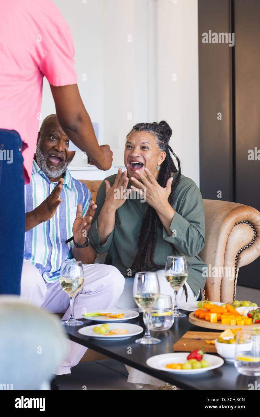 Gli amici festeggiano con gioia con vino e spuntini nell'accogliente salotto Foto Stock