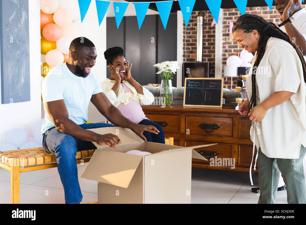 Una coppia in attesa di aprire una confezione regalo presso la baby shower, circondata da amici gioiosi Foto Stock