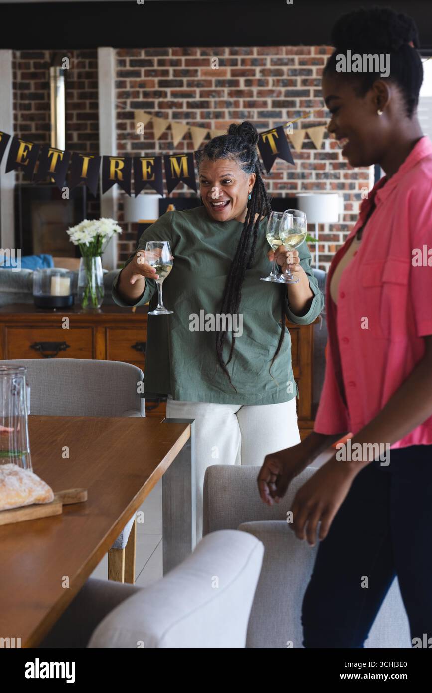 Donna gioiosa che tiene in mano bicchieri da vino per festeggiare la pensione a casa con gli amici Foto Stock