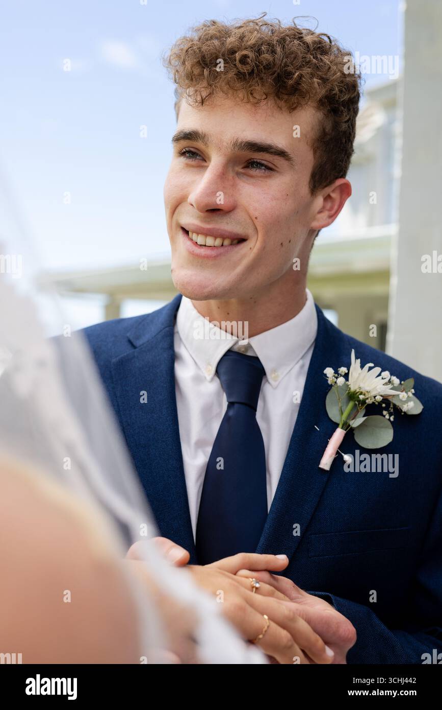 Sposo in tuta blu sorridente calorosamente durante la cerimonia di nozze all'aperto Foto Stock