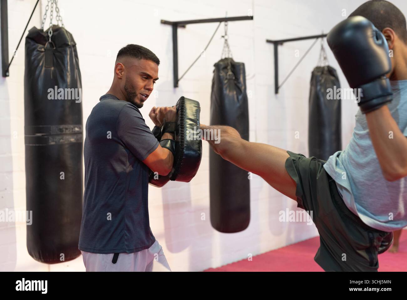 Allenatore afroamericano con allenamento studentesco in palestra con kick pad curvo e guanti da boxe neri Foto Stock