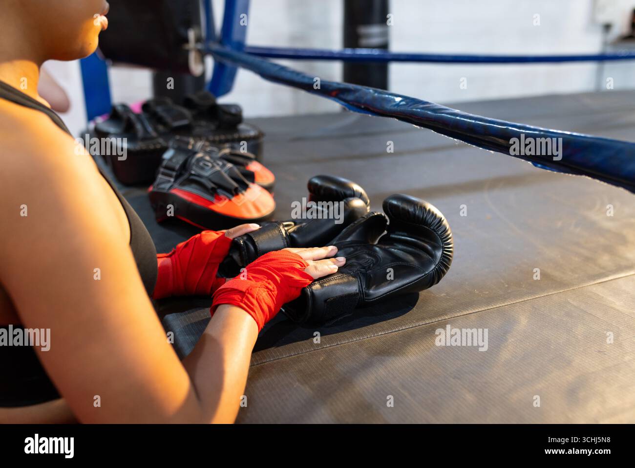 Pugile donna seduta sul bordo dell'anello con guanti neri con involucri rossi, guanti da messa a fuoco Foto Stock