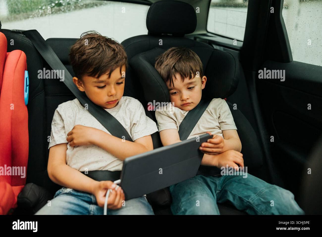 Fratelli che guardano un tablet digitale seduto sul sedile posteriore dell'auto Foto Stock