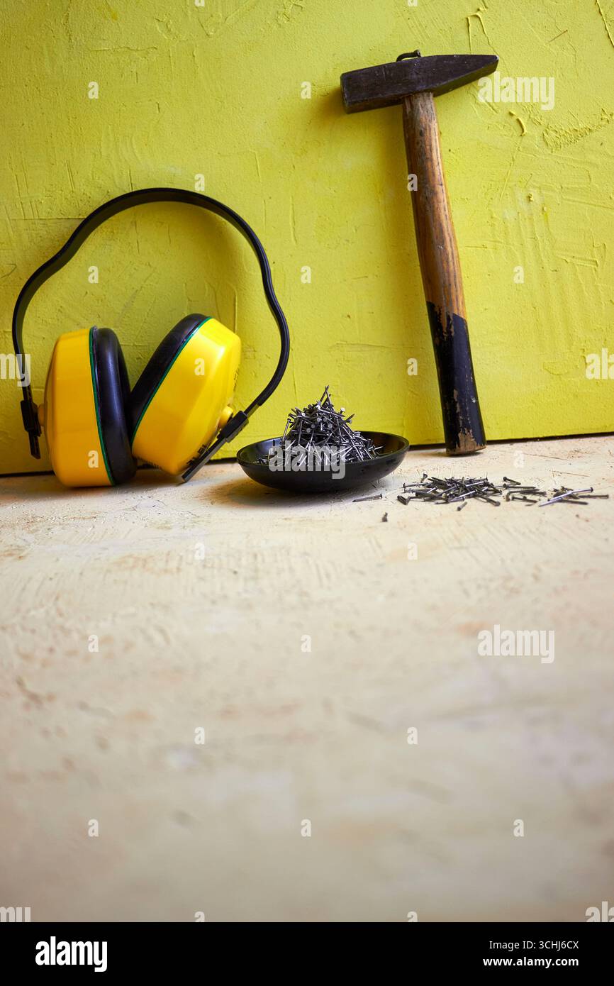 STILL Life con utensili da costruzione: Martello, chiodi in una ciotola di legno e cuffie protettive su uno sfondo giallo a trama. Concetto di costruzione, Foto Stock