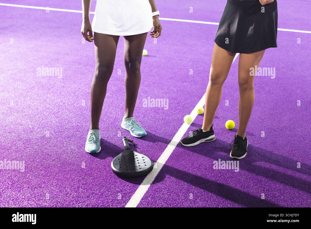 Coppia di donne diverse in piedi sul campo viola con abiti sportivi accanto a pagaia nera e palle gialle Foto Stock