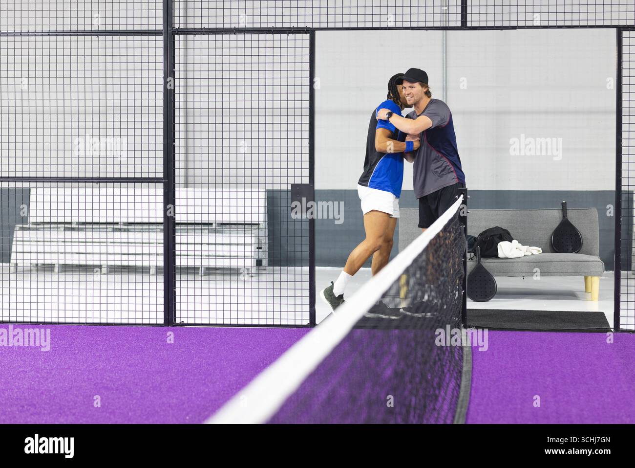 Racchette Padel appoggiate sulla panchina con un asciugamano accanto alla rete sul campo di erba viola in gabbia Foto Stock