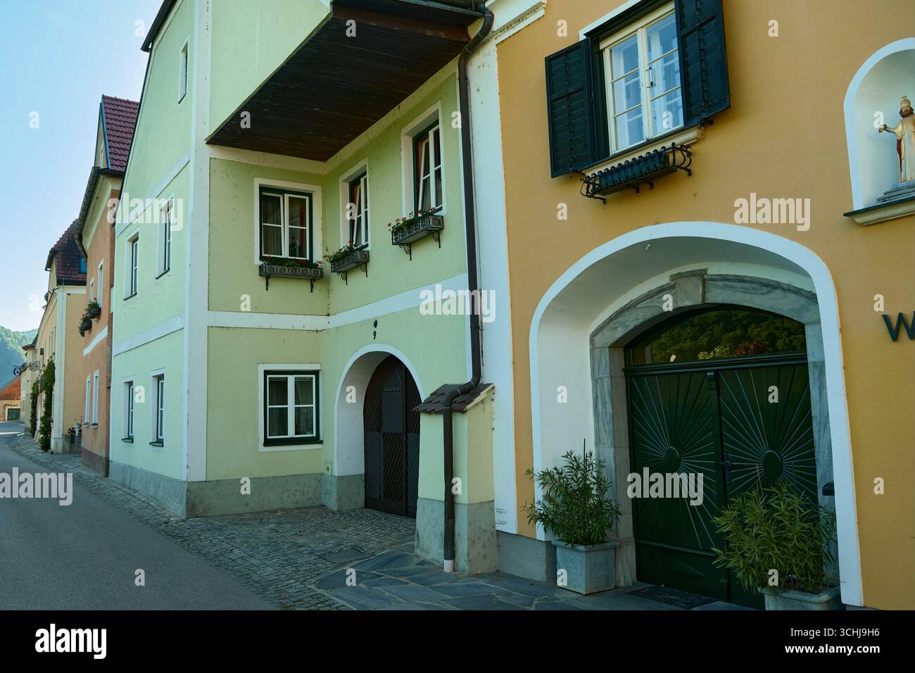Foto di una strada acciottolata a Wachau, Austria. La prima casa è gialla con cancelli verdi e vasi di fiori, seguita da affascinanti case arancioni lungo il Foto Stock
