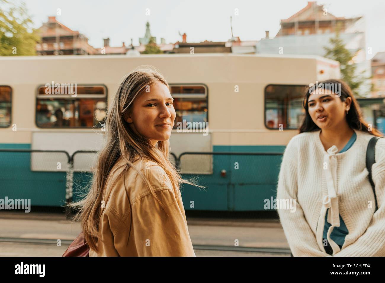 Ritratto di una giovane donna sorridente che guarda a spalla mentre si trova alla fermata del tram in città Foto Stock