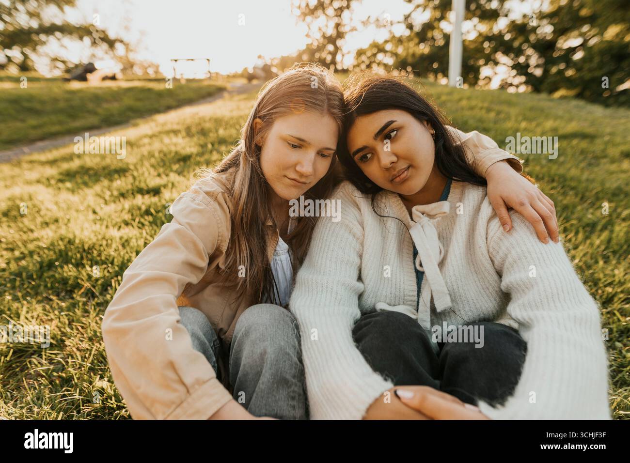 Giovane donna seduta con il braccio intorno a una triste amica sulla collina durante il giorno di sole Foto Stock