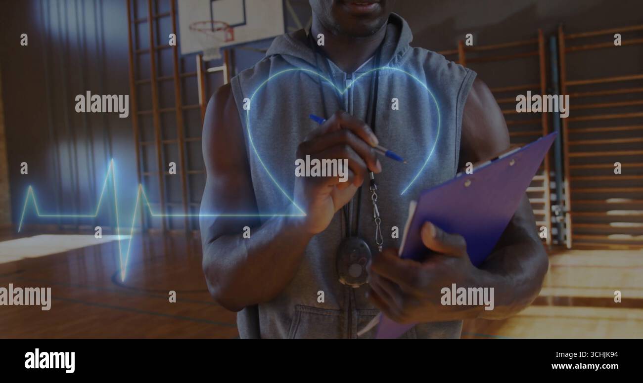 Osservando il fitness coach in felpa con cappuccio che monitora il battito cardiaco sul campo della palestra con fischio e appunti Foto Stock