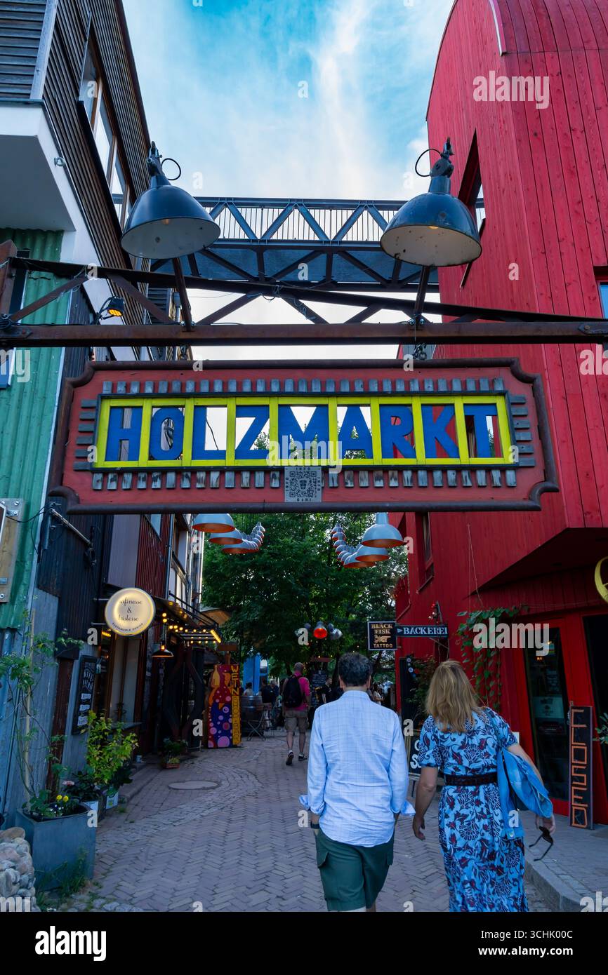 Colorato cartello d'ingresso di Holzmarkt a Berlino con edifici in legno e negozi creativi sullo sfondo in un giorno d'estate (vista verticale). Foto Stock