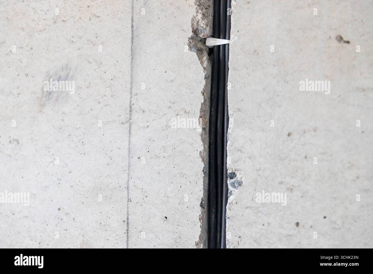 il cavo elettrico è disposto in un corrugamento protettivo nella scanalatura della parete. Fili elettrici e cavi sporgenti nei fori all'interno della parete grigia in cemento per la preparazione Foto Stock