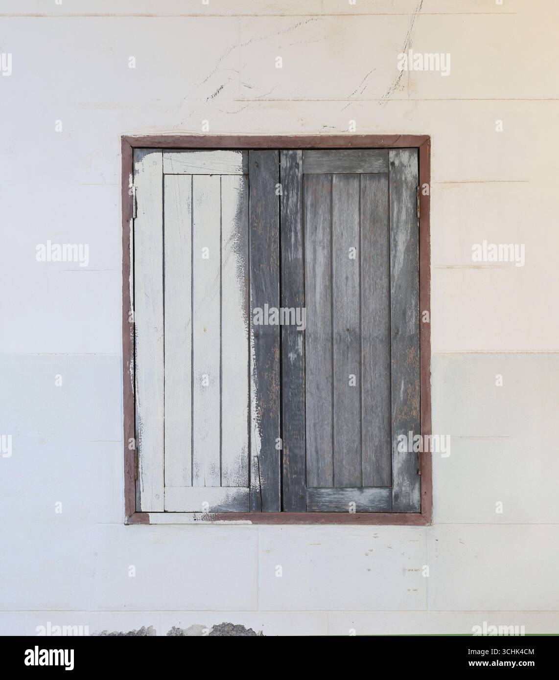 Una finestra in legno intemprato con una finitura in angoscia contrasta con una parete bianca minimalista, evocando un senso di fascino rustico e architettonico Foto Stock