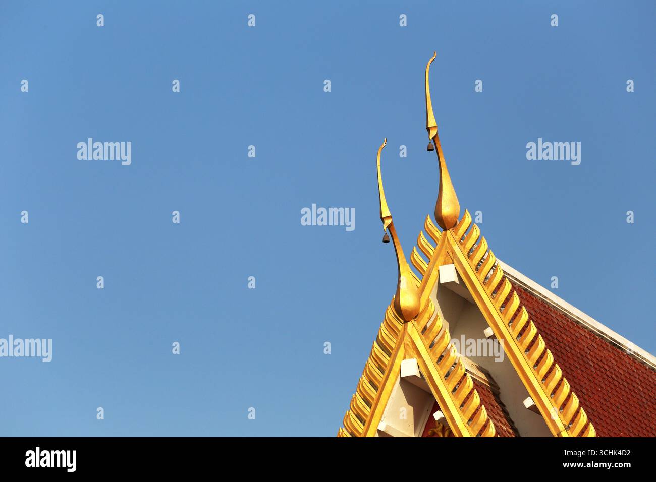 Accattivante dettaglio di un tradizionale tetto di tempio tailandese con picchi dorati ornati che si innalzano su un cielo blu limpido, che incarna l'essenza del cultu Foto Stock
