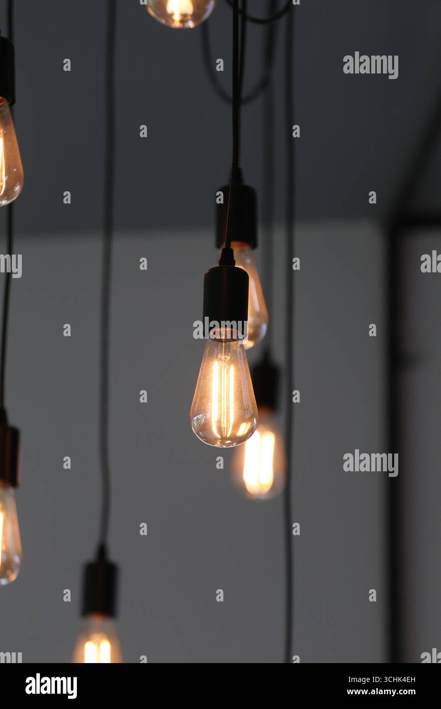 Una collezione di eleganti lampadine a sospensione crea una luce soffusa e calda, che esalta gli interni moderni e aggiunge fascino a qualsiasi ambiente, perfetto per i ristoratori Foto Stock