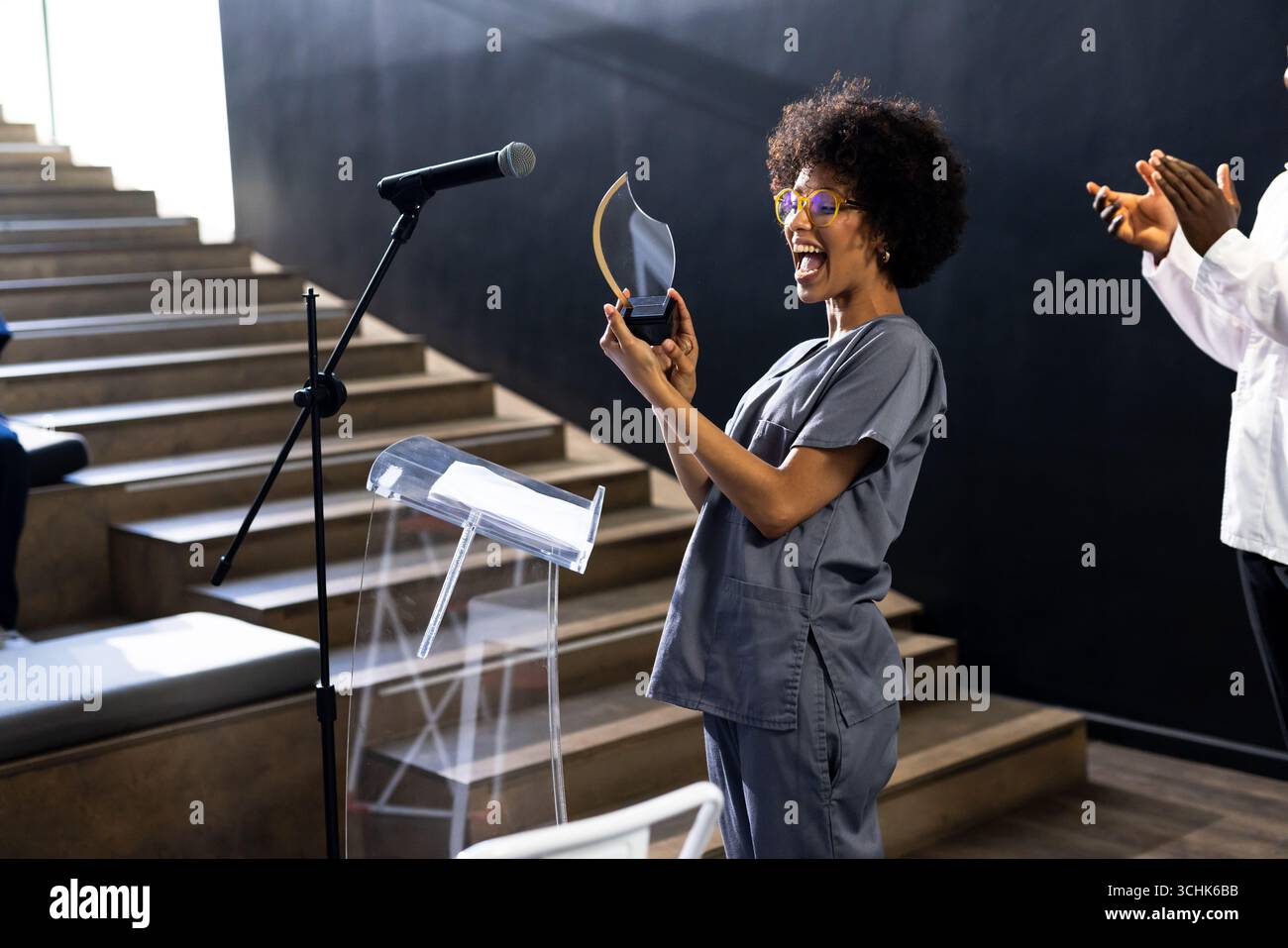 donna in scrub che riceve con gioia un premio sul palco alla conferenza, nella sala conferenze Foto Stock