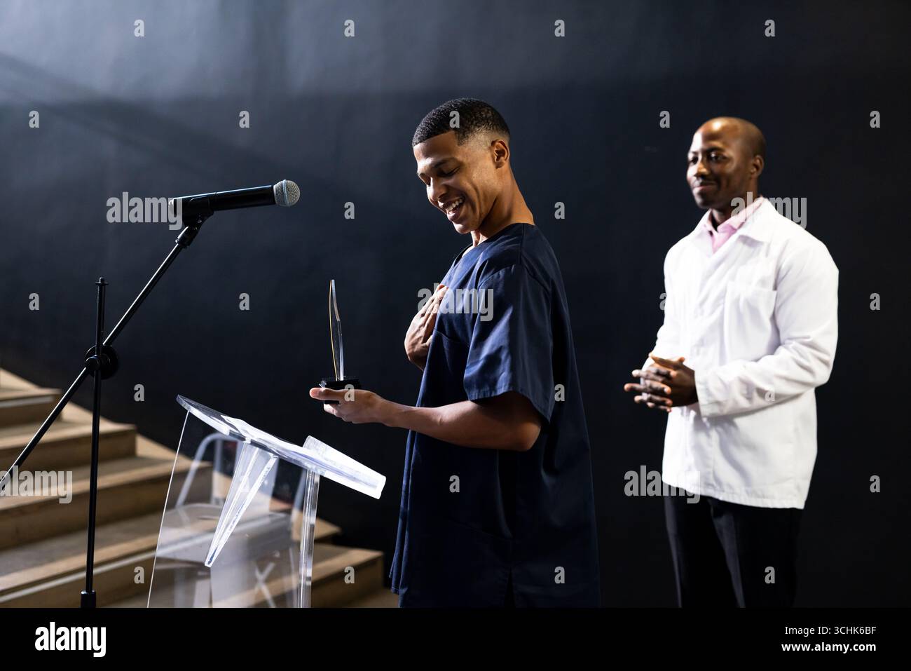 Ricevendo un premio sul palco, un uomo che tiene un trofeo, un collega applaude nelle vicinanze, nella sala conferenze Foto Stock