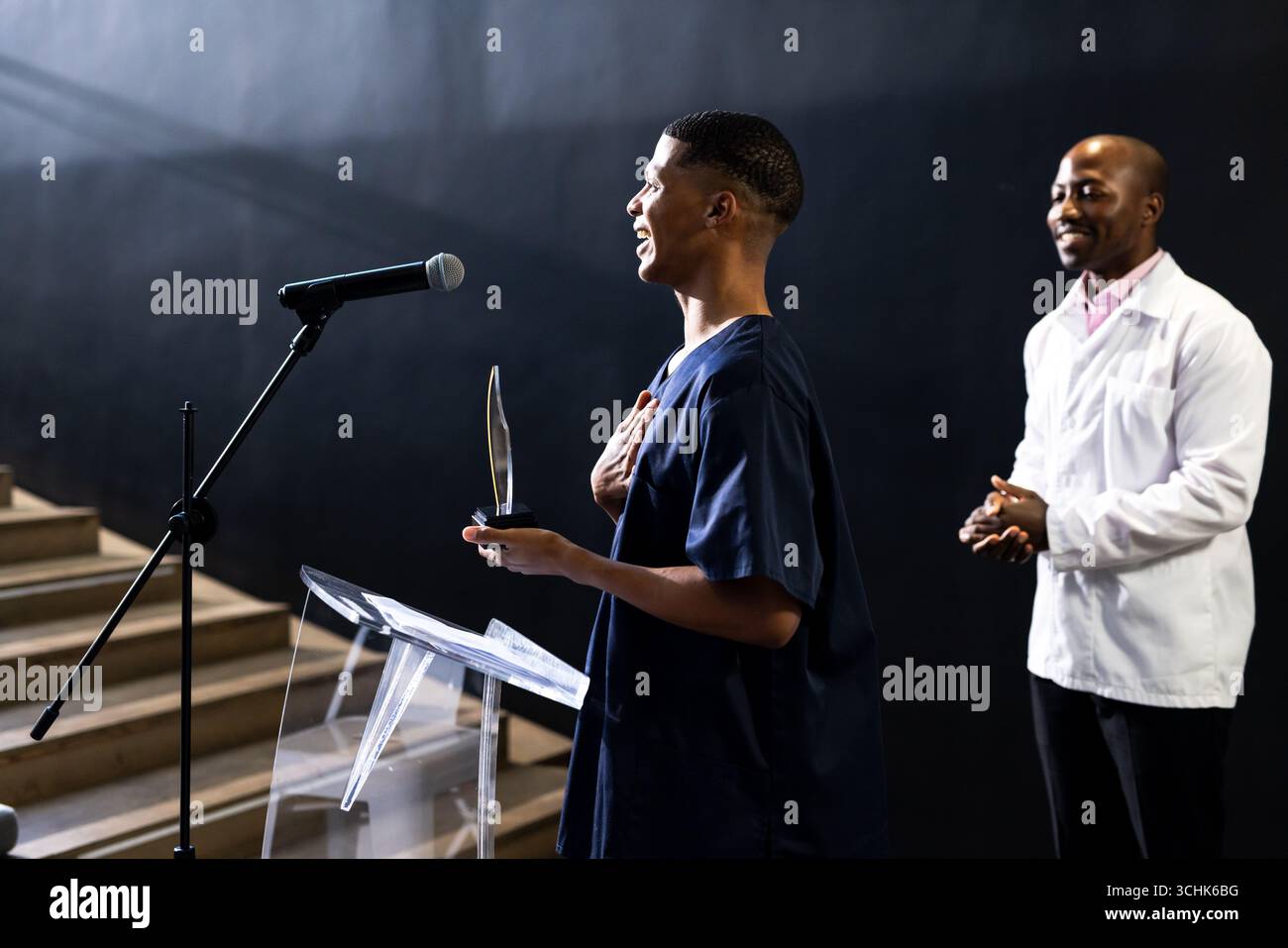 uomo che tiene un premio parlando sul podio, sorridendo con orgoglio, nella sala conferenze Foto Stock