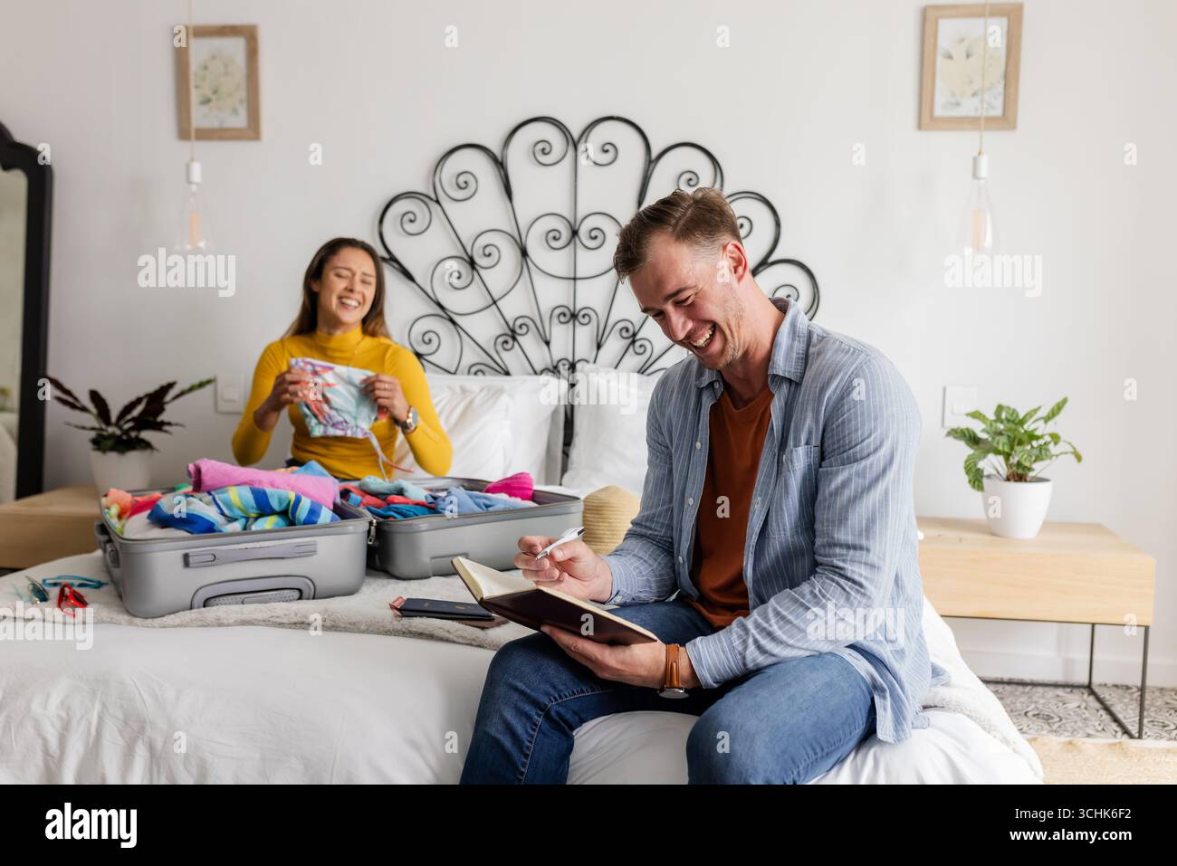 Coppia che prepara la valigia sul letto, sorridendo e pianificando una vacanza insieme Foto Stock