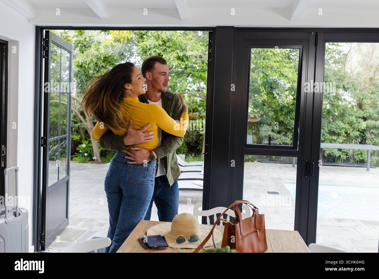 Una coppia si abbraccia con gioia a bordo piscina, godendosi una giornata di sole a casa Foto Stock