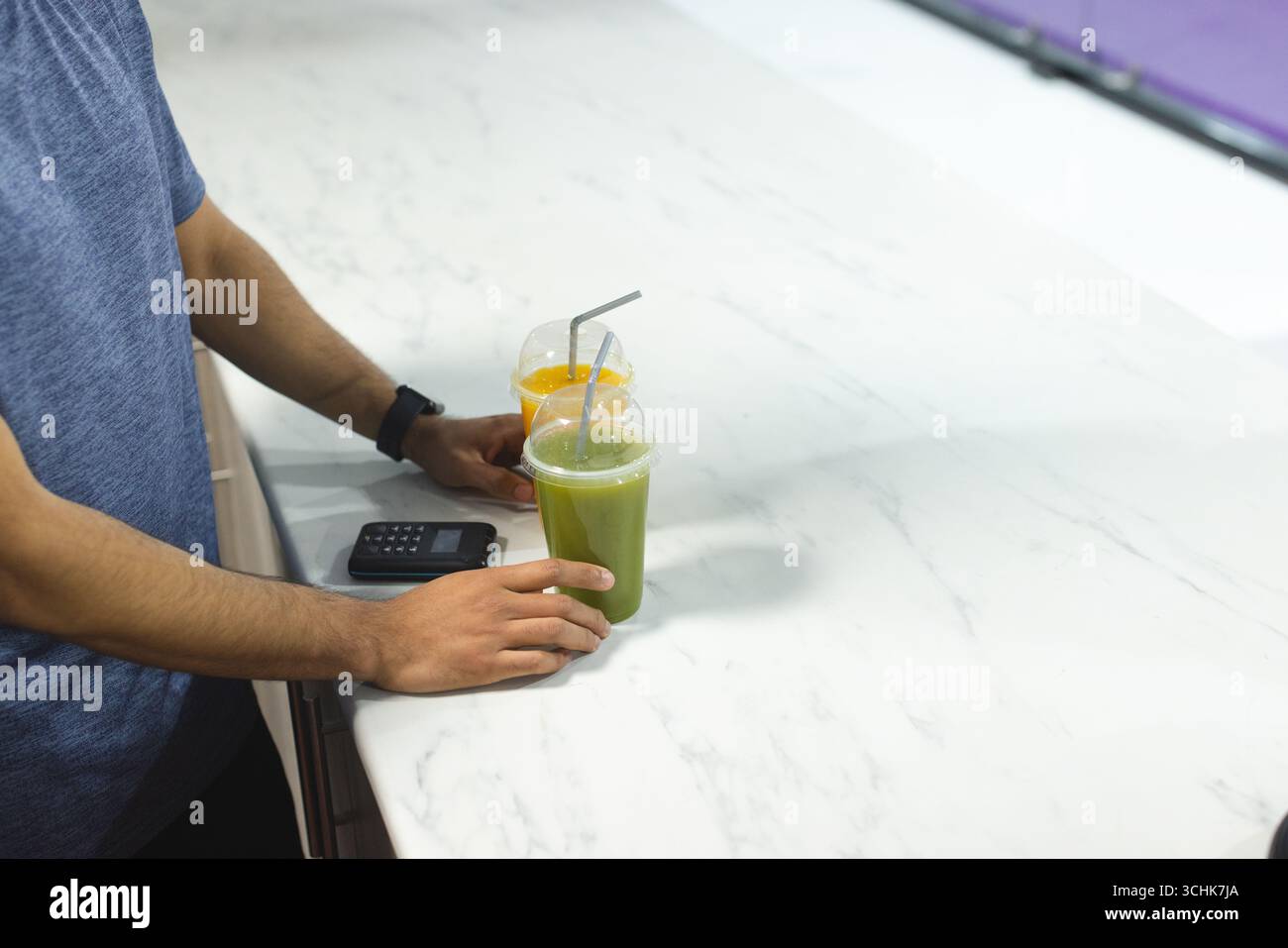 Uomo in piedi al banco del Juice bar con due bicchieri di plastica accanto al terminale di pagamento con carta, spazio per fotocopie Foto Stock