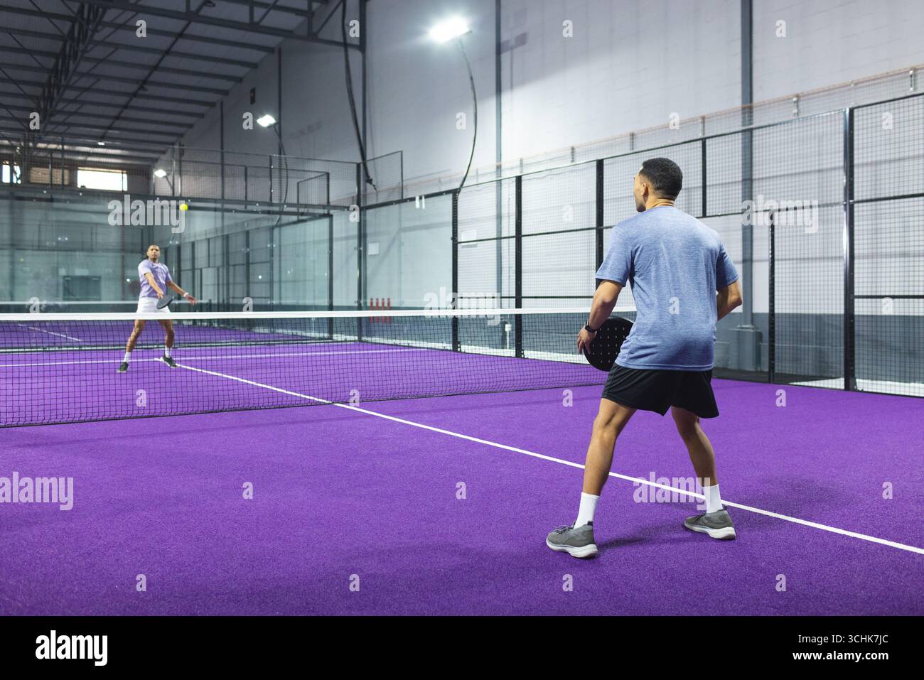 Diversi atleti maschili che gareggiano su un campo da padel viola in una struttura sportiva con racchette e spazio per copiare Foto Stock