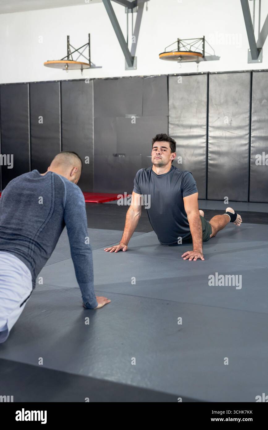 I partner maschili che si allenano con la schiena si allungano sui tappetini in palestra con piattaforme Speed bag Foto Stock