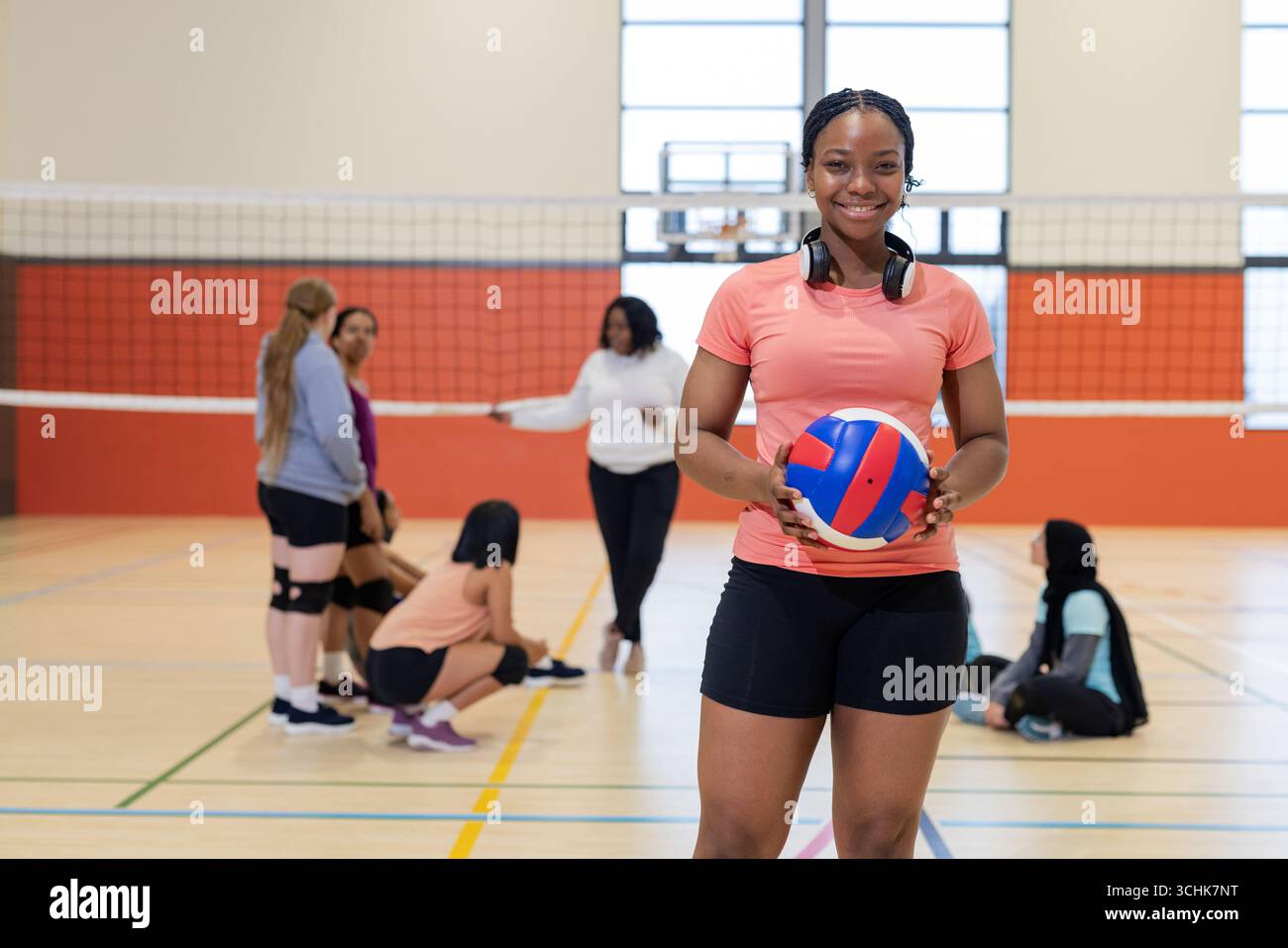 Donna indiana con t-shirt in corallo in piedi sul campo con pallavolo con cuffie, spazio copia Foto Stock