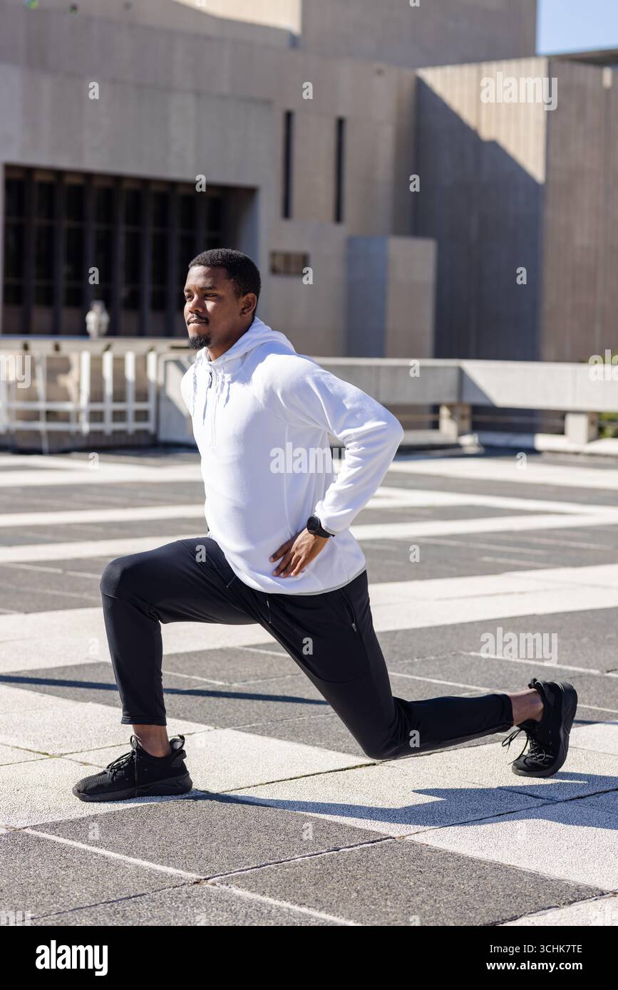 Uomo afro-americano che si affonda in avanti sulla piazza esterna piastrellata con smartwatch sportivo a controllo Foto Stock