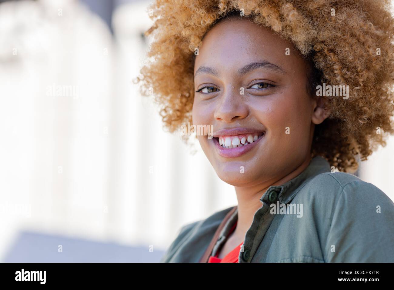 Donna afroamericana in posa, sorridente fuori dal campus in camicia verde sopra la maglietta rossa, copia spazio Foto Stock
