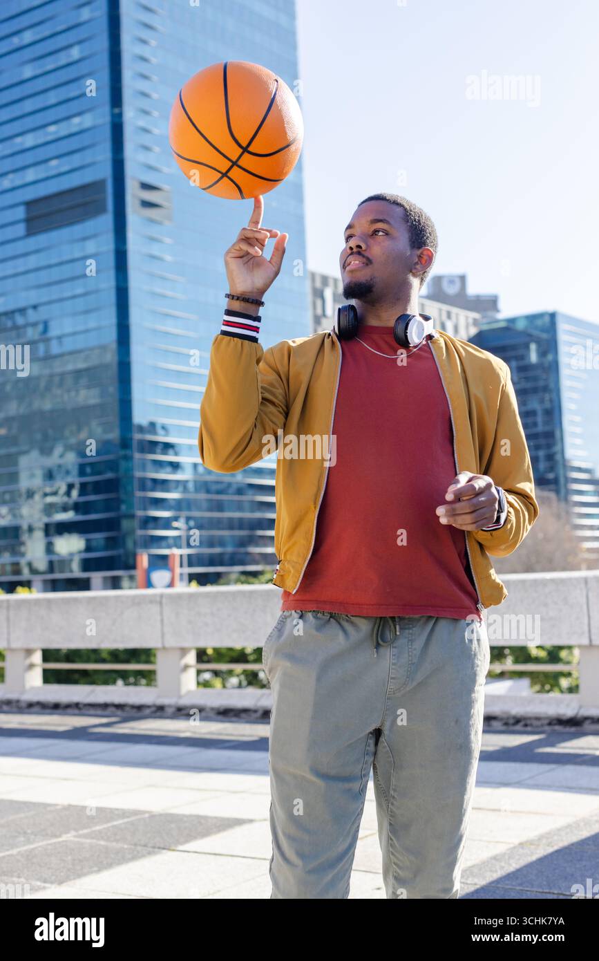 Uomo afro-americano che gioca a basket al dito in plaza con le cuffie da bomber Foto Stock