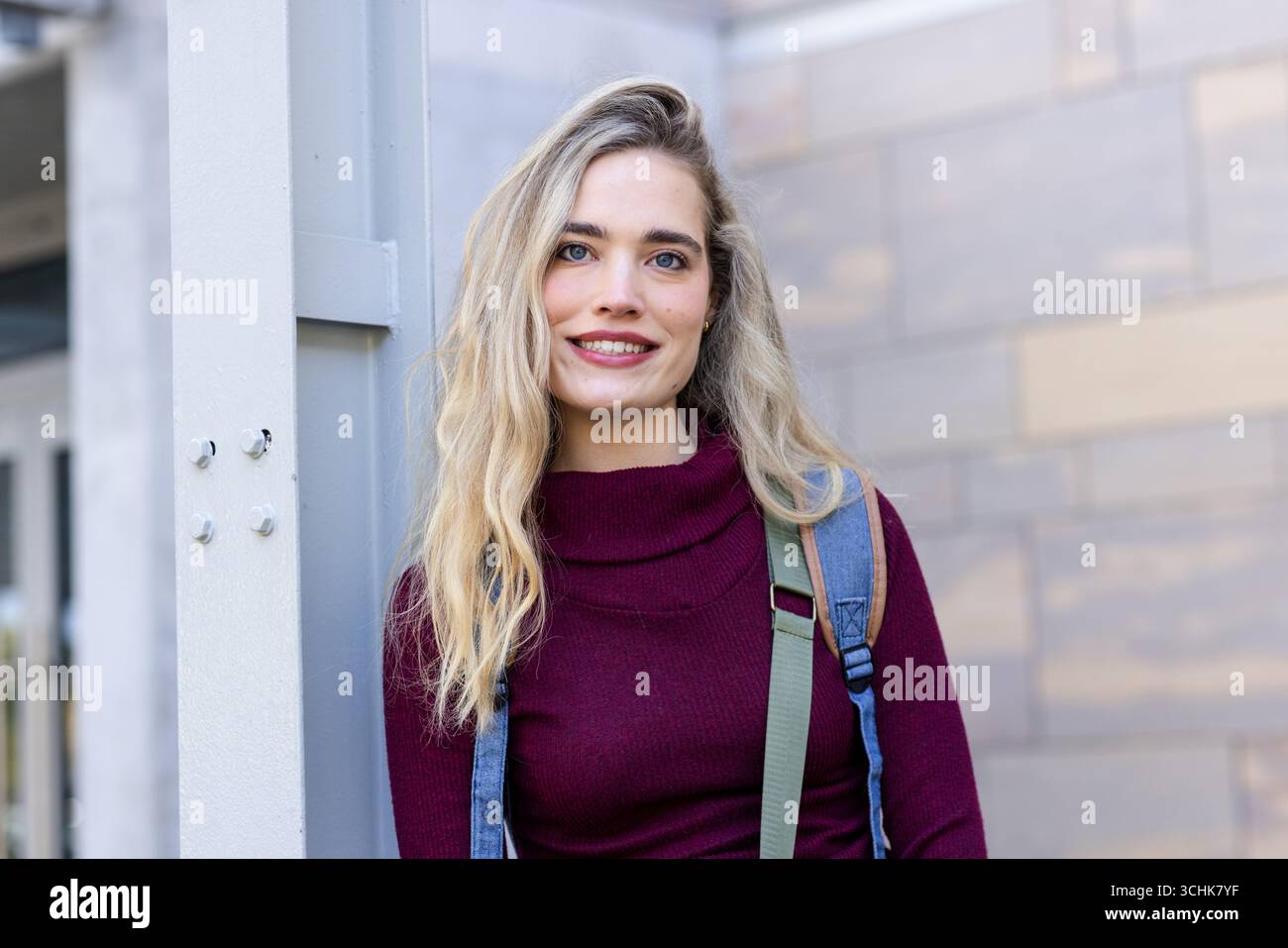 Donna appoggiata su una colonna di supporto in metallo all'esterno dell'edificio con piano Borgogna con zaino Foto Stock