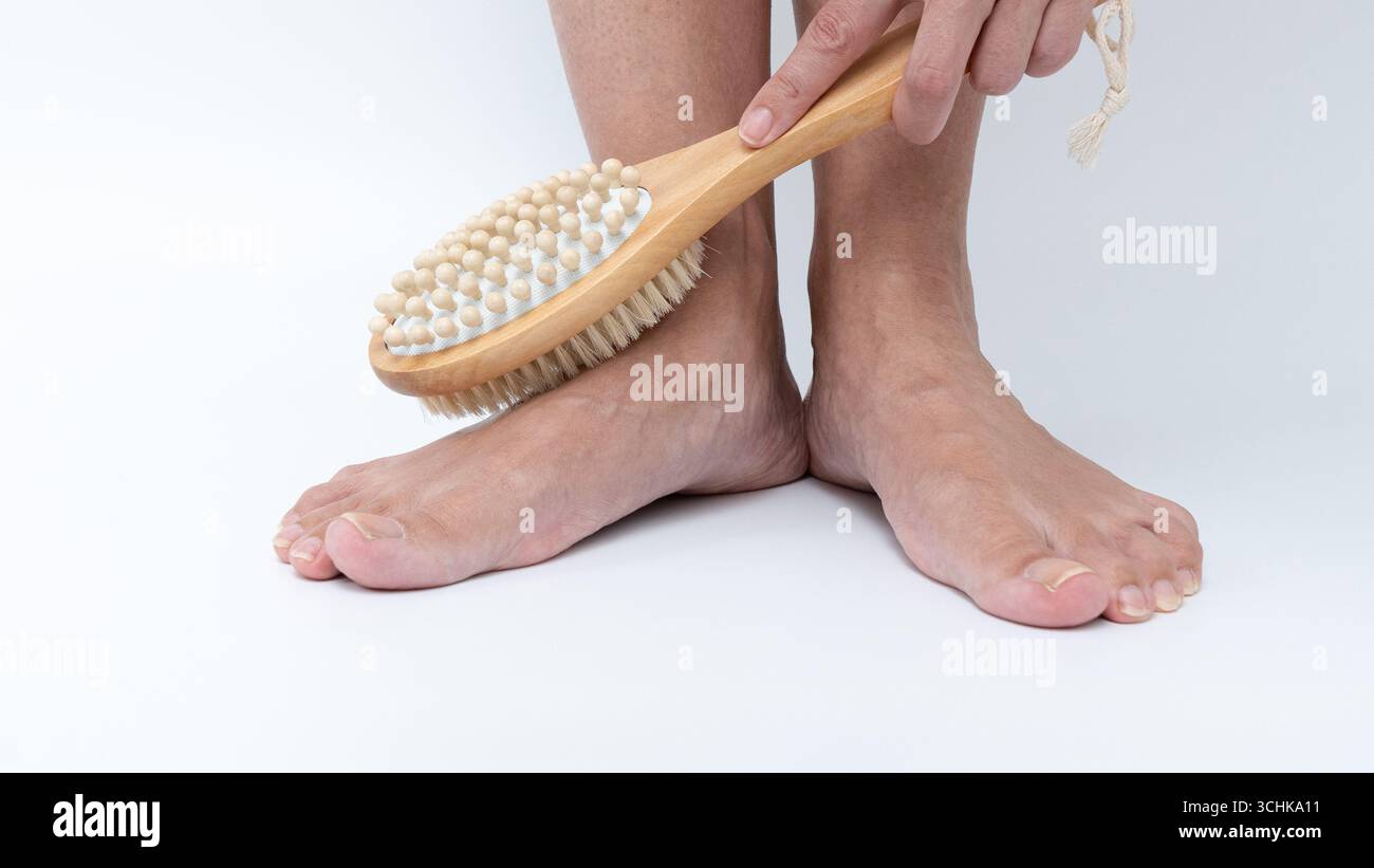 Gambe e piedi stanchi vengono spazzolati con una spazzola per il corpo in legno, che enfatizza le tecniche di cura e rilassamento per gli arti dolorosi e pesanti Foto Stock