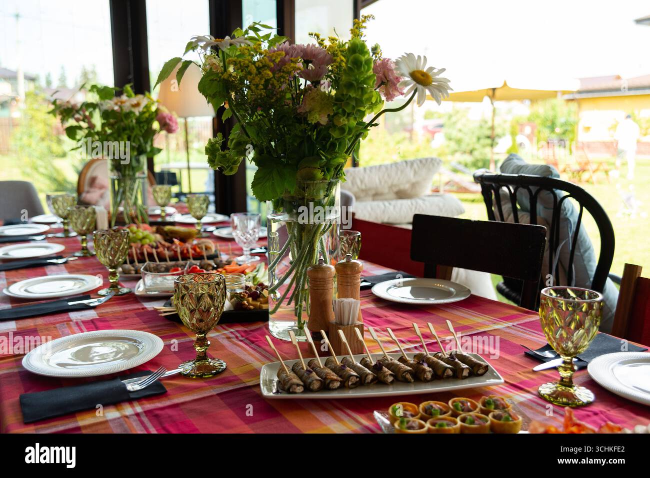 Un tavolo splendidamente decorato per una festa in giardino all'aperto. l'allestimento include composizioni floreali, eleganti bicchieri e una varietà di antipasti, Foto Stock