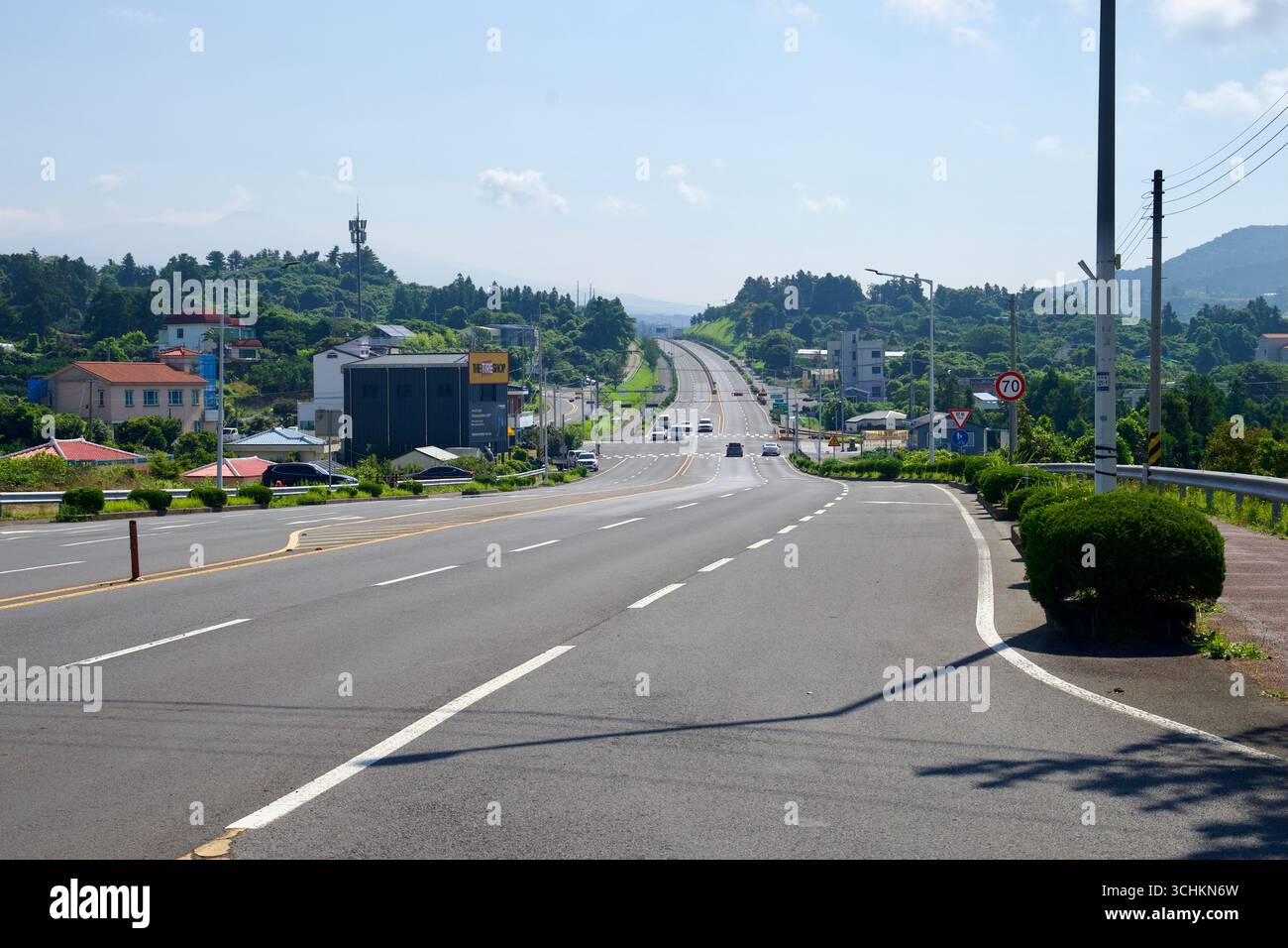 Una lunga vista lungo Iljuseo Road mostra l'autostrada divisa che passa davanti a case e piccole imprese verso basse colline boscose, con traffico leggero e a c Foto Stock