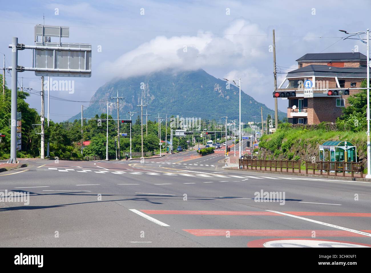 I semafori e i lampioni incorniciano una vista distante del monte Sanbang sotto una nuvola di capote, vista lungo un'arteria urbana con più corsie, mediane, Foto Stock