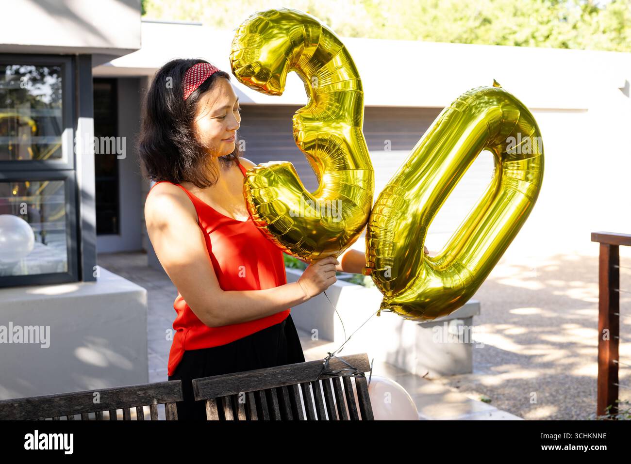 Alla festa, donna che tiene in mano palloncini d'oro per celebrare il 30° compleanno sul ponte, sorridendo con gioia Foto Stock