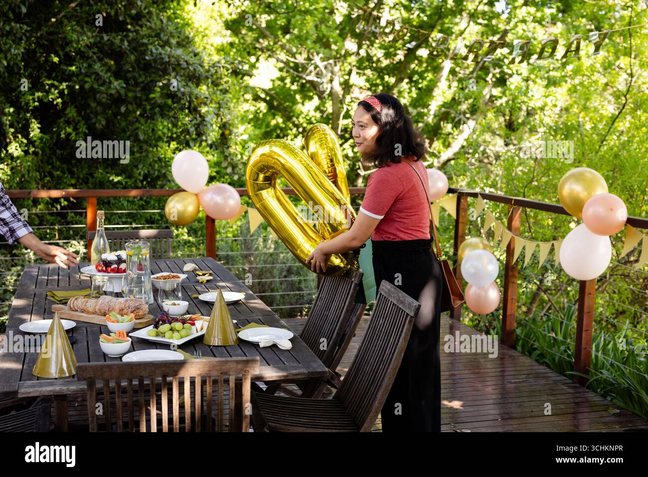 Alla festa, donna con palloncini d'oro che si prepara al tavolo della festa di compleanno sul ponte Foto Stock