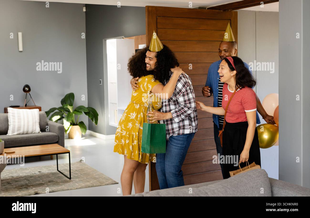 Alla festa, amici diversi che celebrano una festa a sorpresa a casa, abbracciano e sorridono con gioia Foto Stock