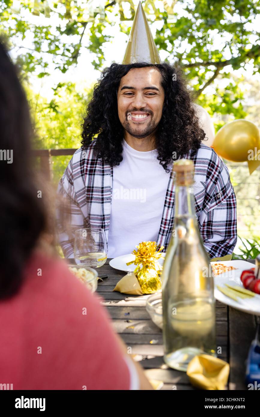 Alla festa, un uomo sorridente che indossa un cappello da festa e si diverte a festeggiare sul ponte con diversi amici Foto Stock