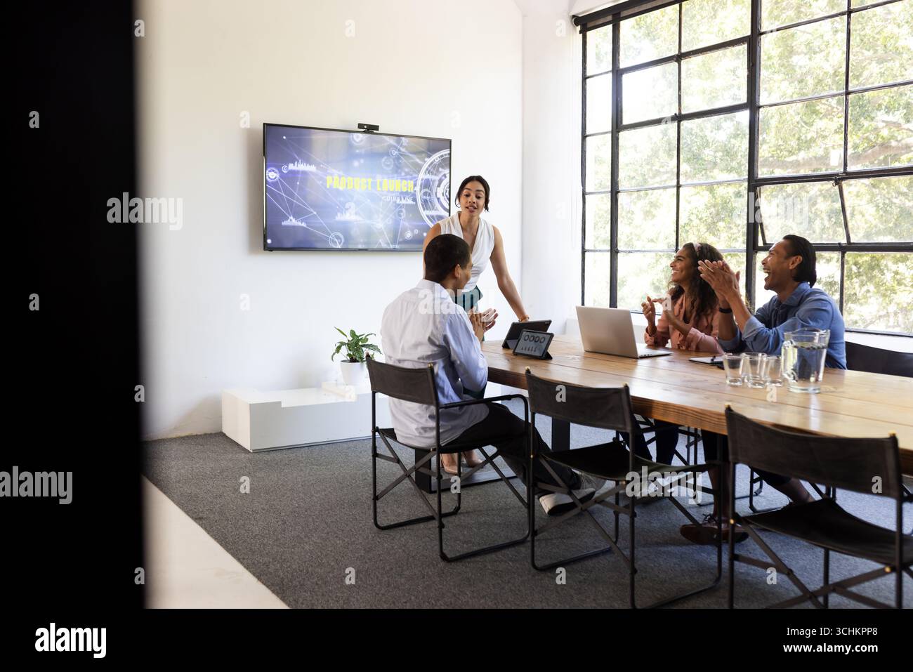 In un ufficio moderno, un team eterogeneo che utilizza un laptop e una schermata di presentazione per la discussione dei progetti Foto Stock