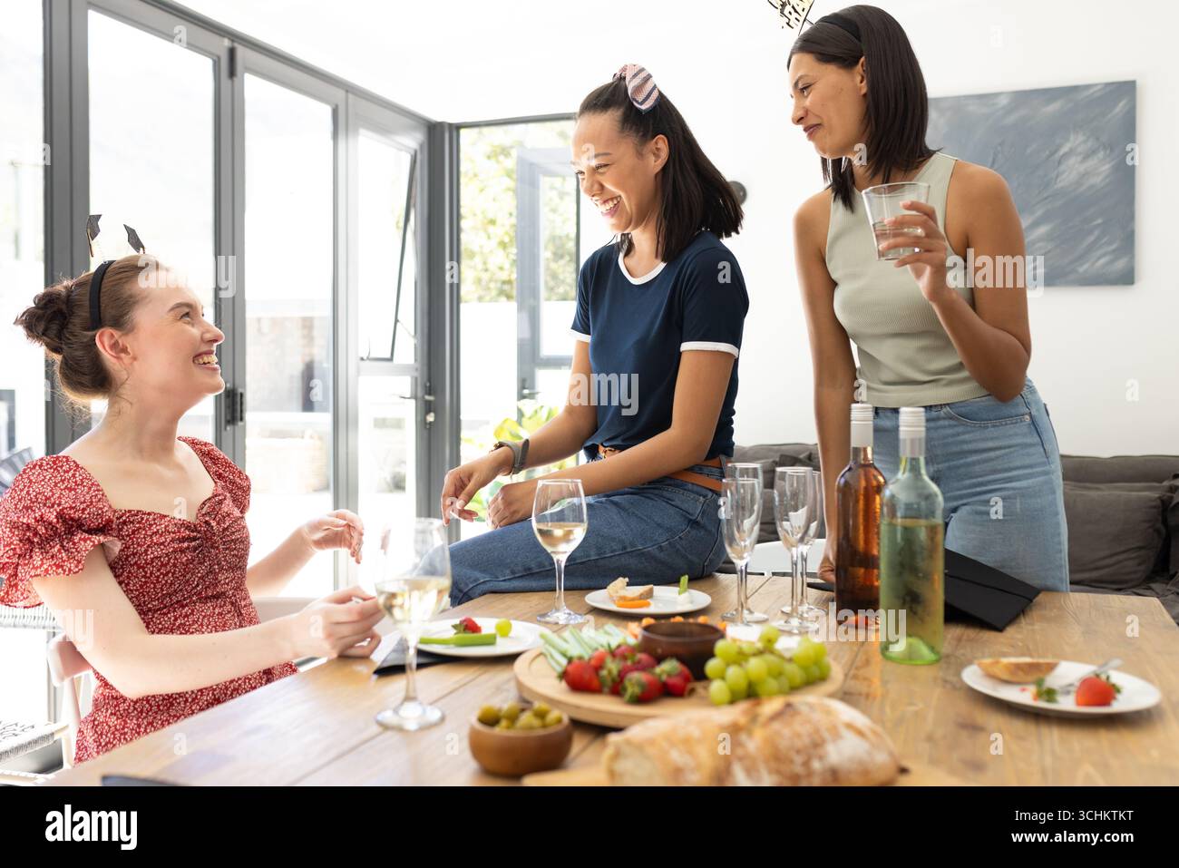 Ridendo e chiacchierando, tre giovani donne si godono il pomeriggio di sole riunirsi a casa Foto Stock